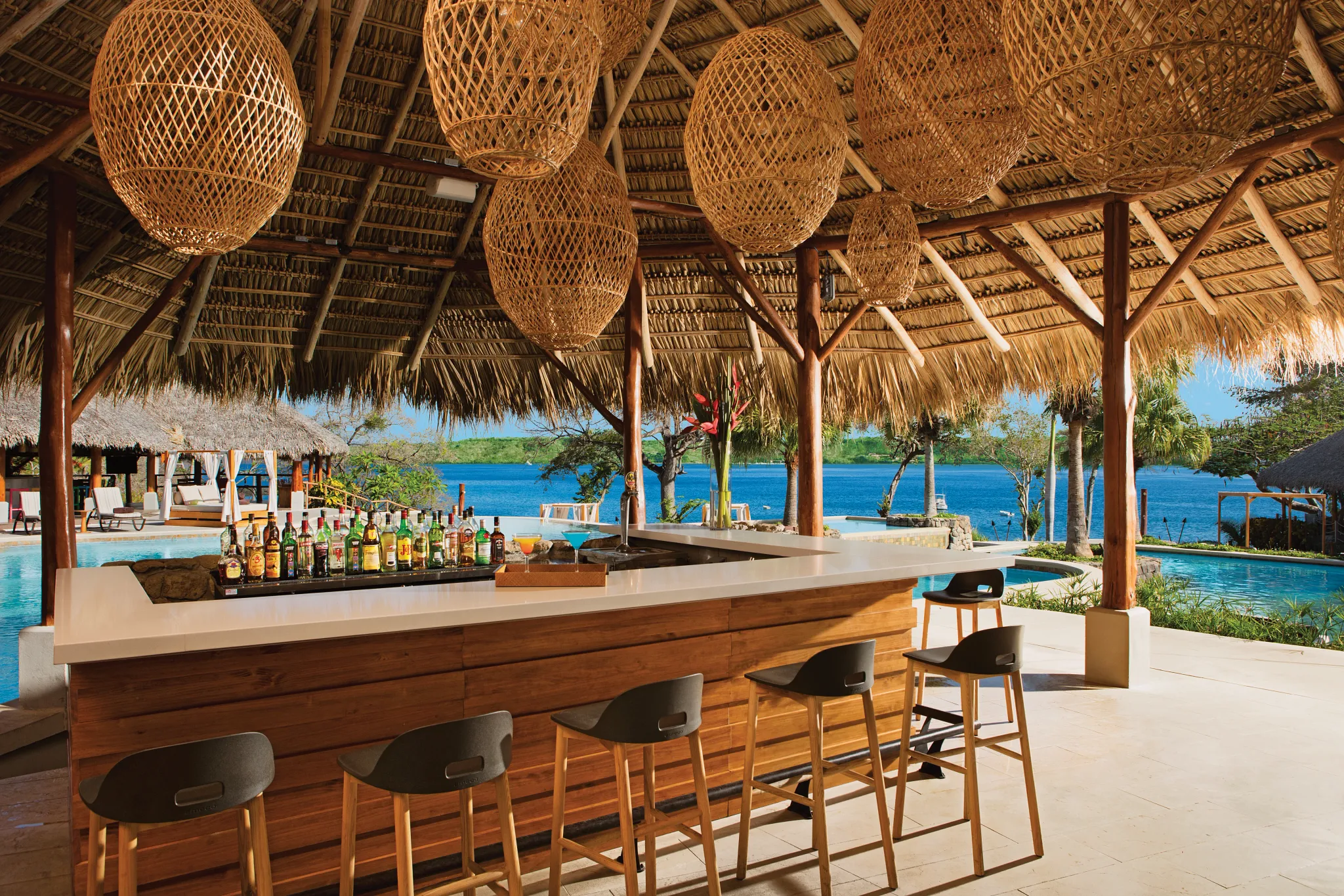 Manatees Swim-Up Bar at Secrets Papagayo Costa Rica featuring a tropical open-air bar with thatched roof, woven pendant lights, poolside seating, and ocean views.
